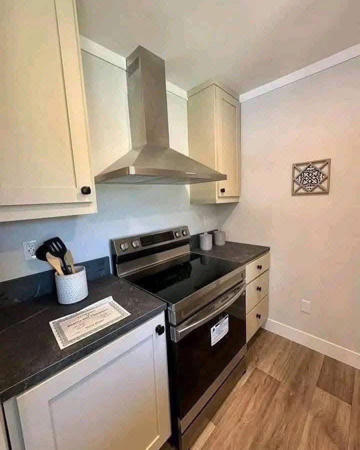 Modern kitchen with light cabinetry and a stainless steel oven under a sleek range hood. Black countertop holds utensils, adding a tidy, minimalist feel.