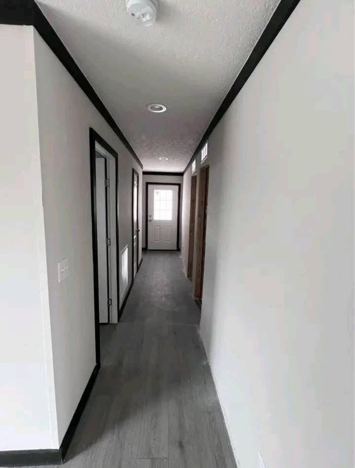 Long hallway with gray wooden floor and white walls, featuring several doors and a distant door at the end letting in light, creating a bright, clean atmosphere.