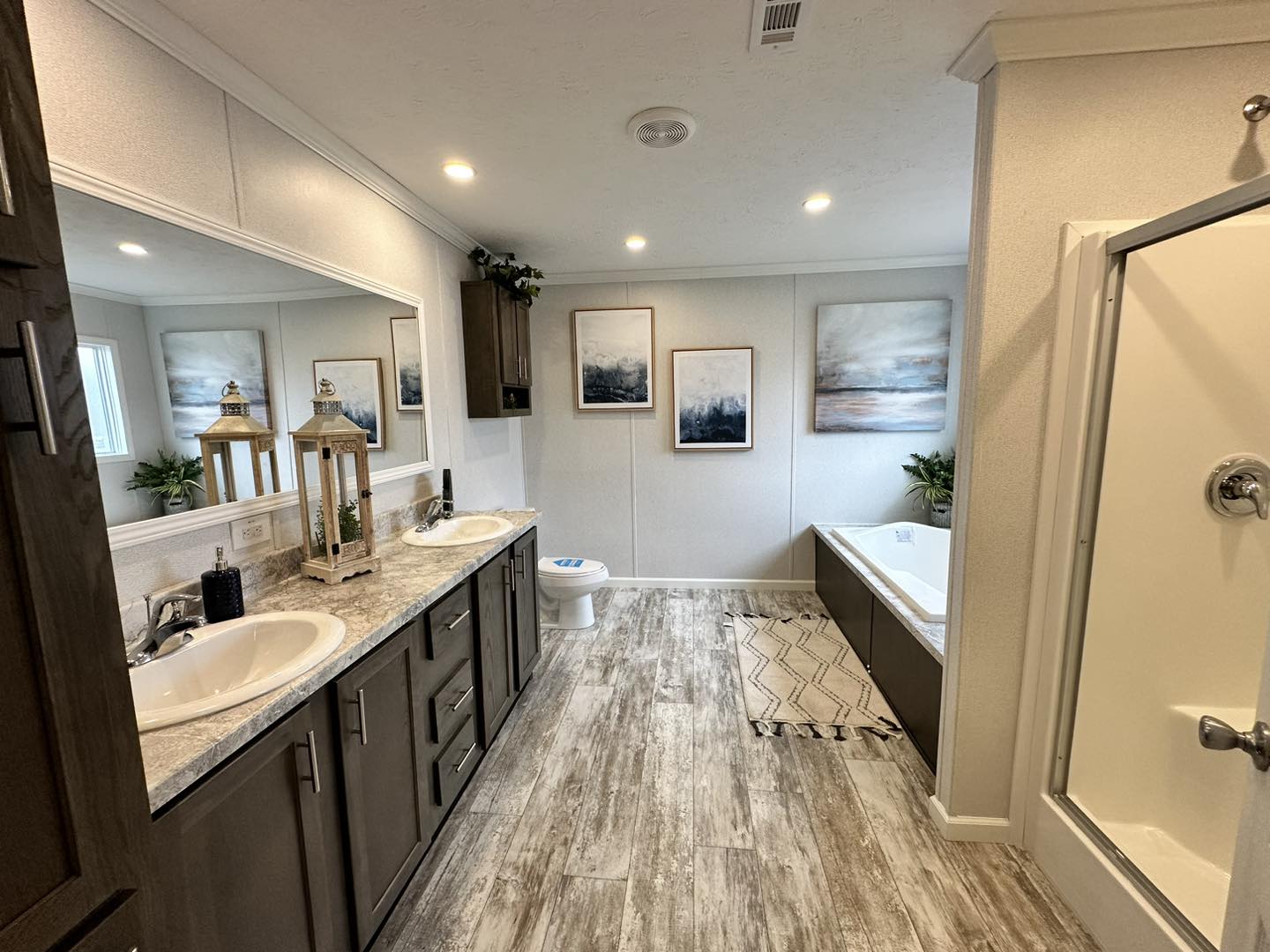 Modern bathroom with dual sinks, wooden cabinets, and decorative lanterns. Features a bathtub, shower, abstract art, and light wood flooring. Serene ambiance.