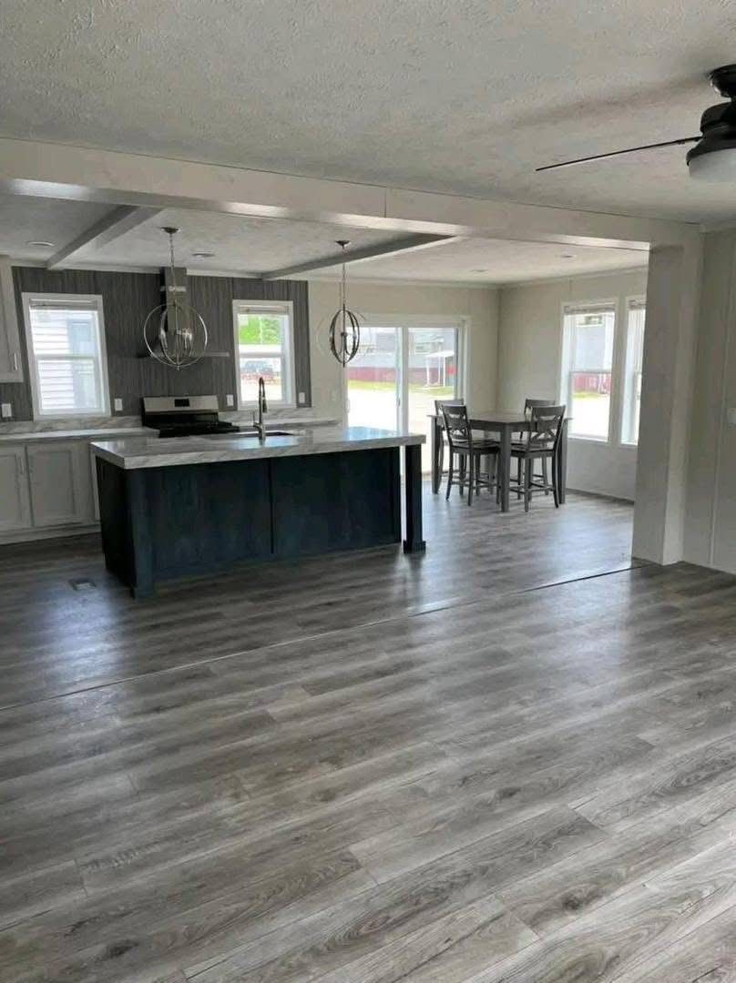 Spacious modern kitchen with wood floors, large central island, pendant lights, and adjacent dining area. Bright with natural light from multiple windows.