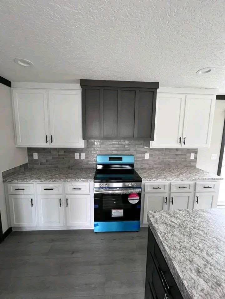 Modern kitchen with white cabinets, gray backsplash, and stainless steel oven. Granite countertops and a contrasting dark hood add elegance.