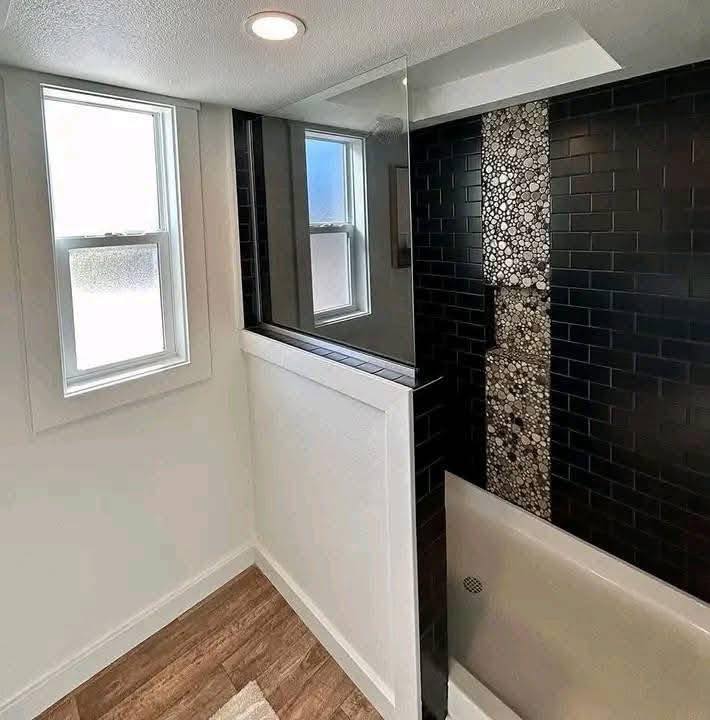 Modern bathroom with a black tiled shower and pebble accent strip. White walls and natural light from a window create a bright, clean atmosphere.