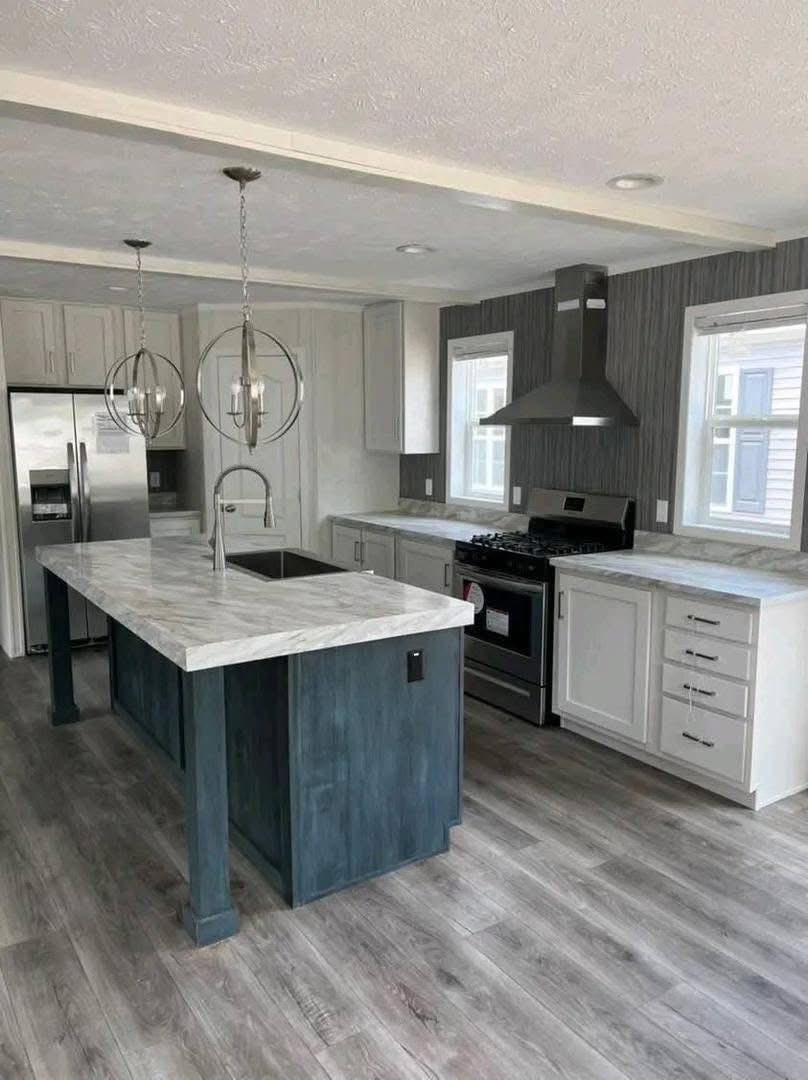 Modern kitchen with gray flooring, a large island featuring a marble countertop, and blue base. Stainless steel appliances, pendant lights, and white cabinets create a sleek, contemporary feel.