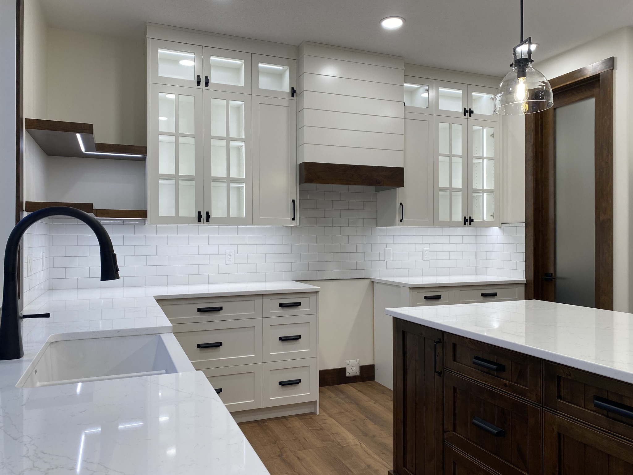 Modern kitchen with white cabinets and dark accents, featuring glass-paneled doors. Spacious countertops, subway tile backsplash, and wood flooring.