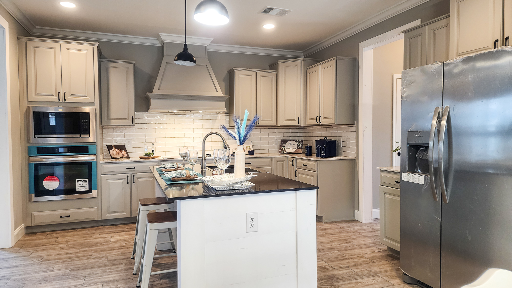 Modern kitchen with beige cabinets, stainless steel appliances, and a central island with barstools. Bright lighting and a clean, welcoming atmosphere.