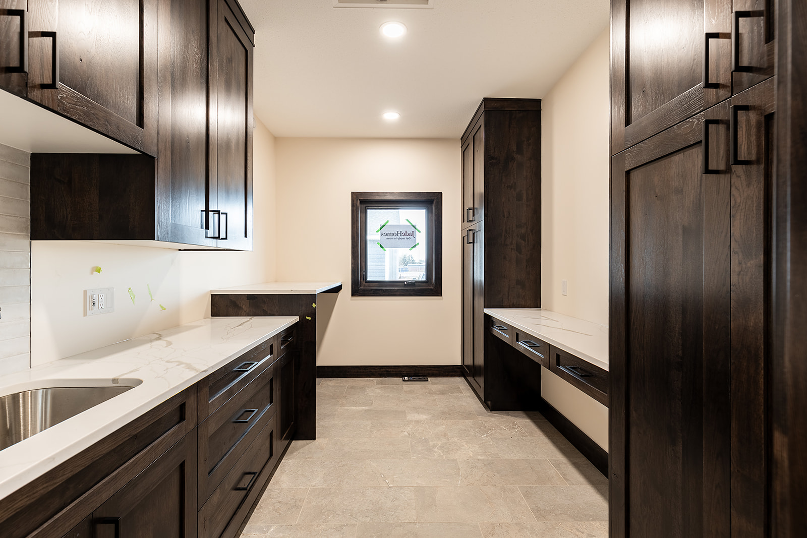 Spacious laundry room with dark wood cabinets and marble countertops. Neutral tones and recessed lighting create a modern, elegant atmosphere.