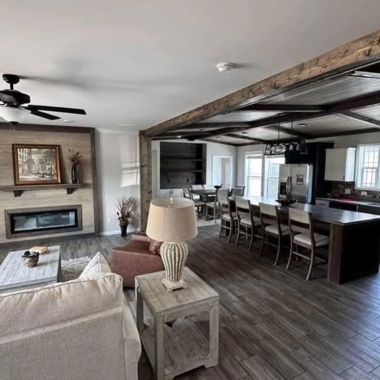 Spacious living area with wooden floors, a beige sofa, and a stone fireplace. Modern kitchen with a long dark countertop and barstools. Earthy tones.