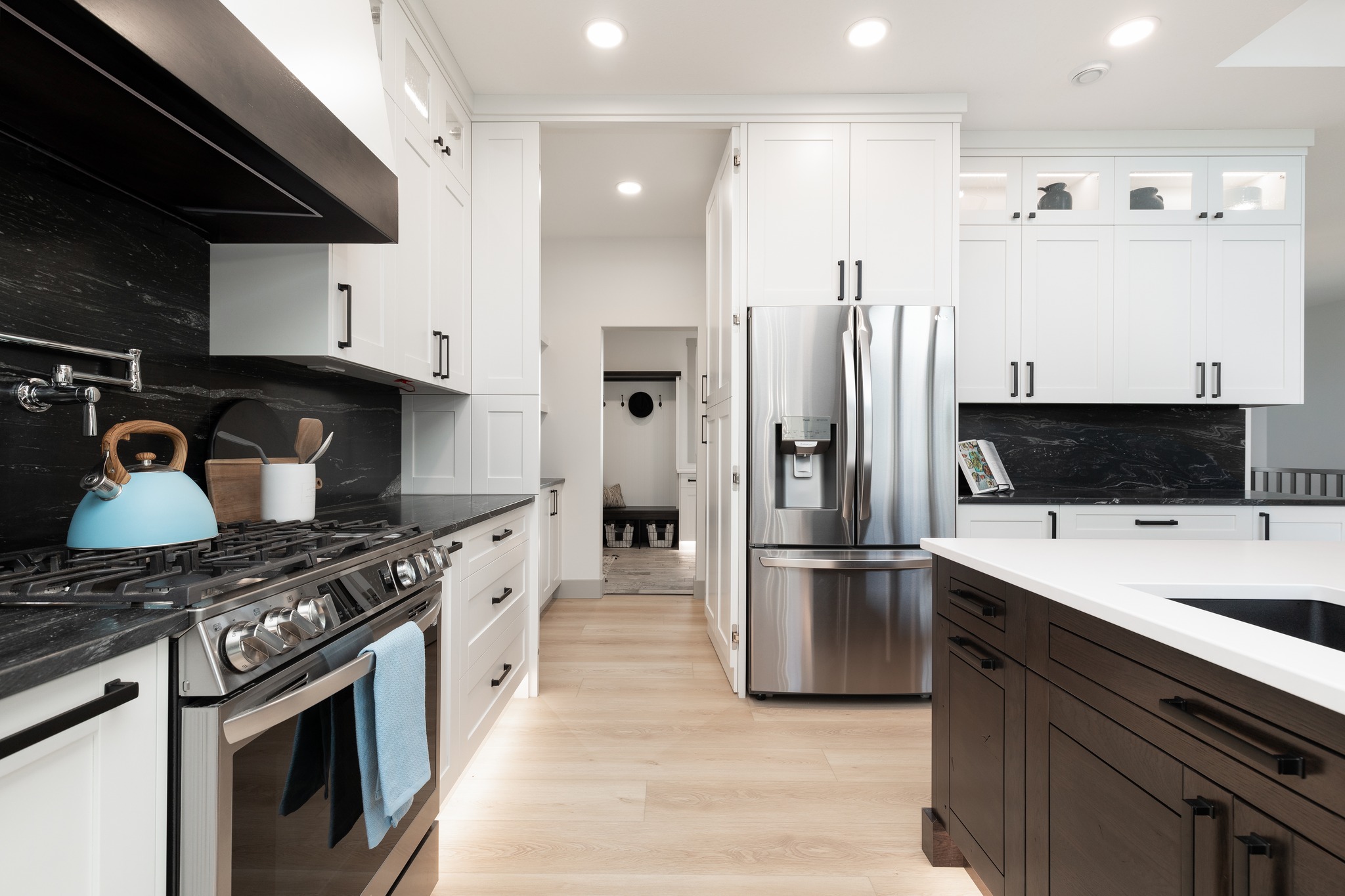 Sleek modern kitchen with white cabinets, black countertops, a stainless steel fridge, and a stove. Bright lighting and a relaxed, contemporary feel.