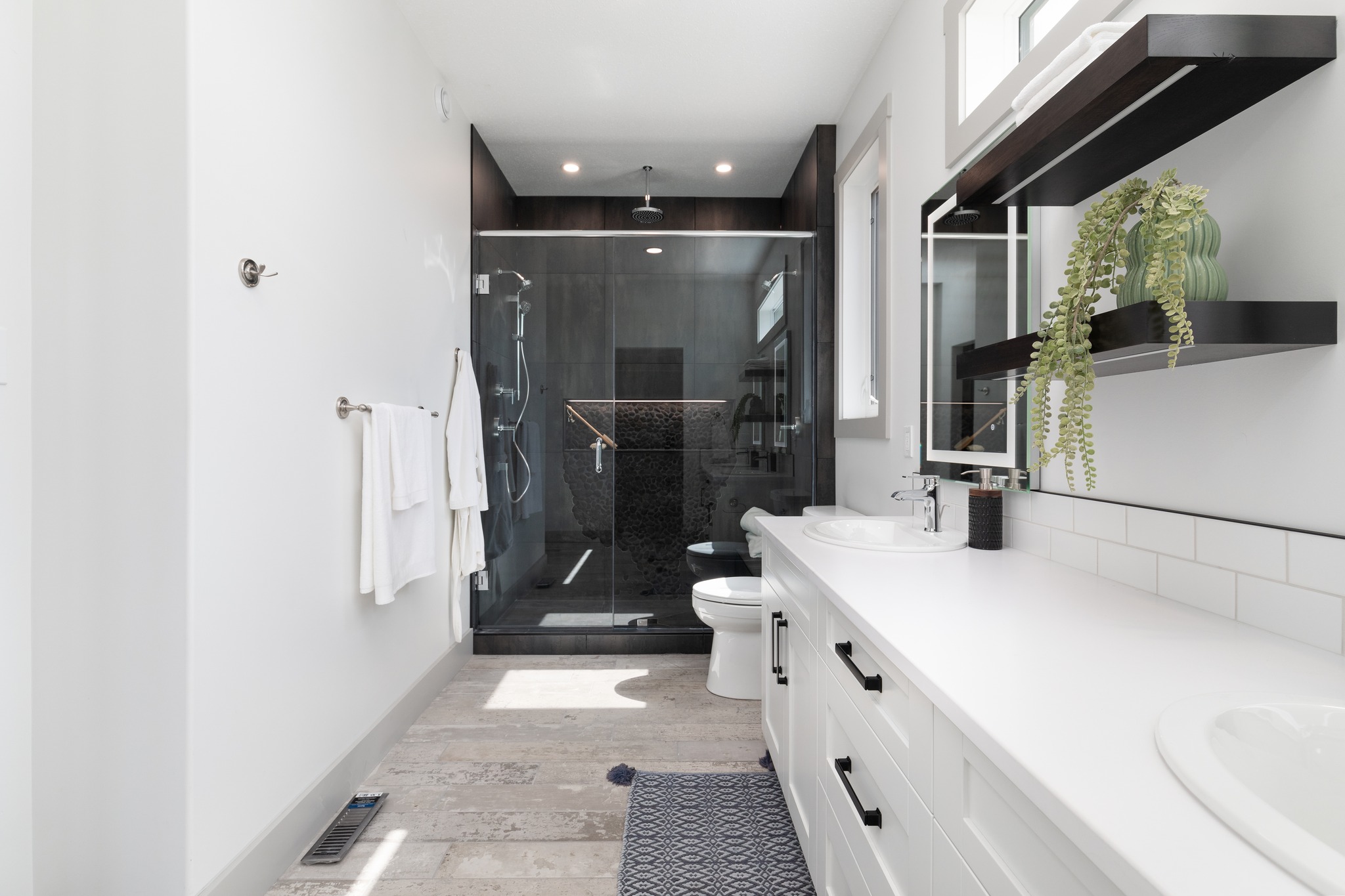 A modern living room with large, triangular windows lets in natural light, highlighting the brown sofa, armchairs, and a dark fireplace. The room is airy and elegant.