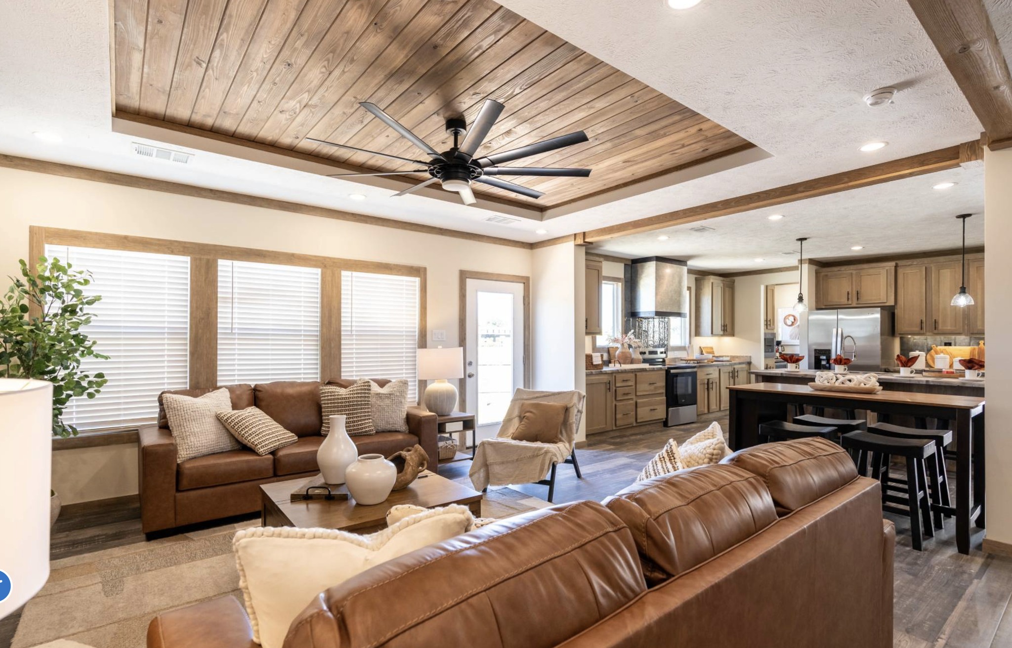 Modern kitchen and dining area with wood accents, featuring a large island with a sink and pendant lights, open to a cozy living room with a TV.
