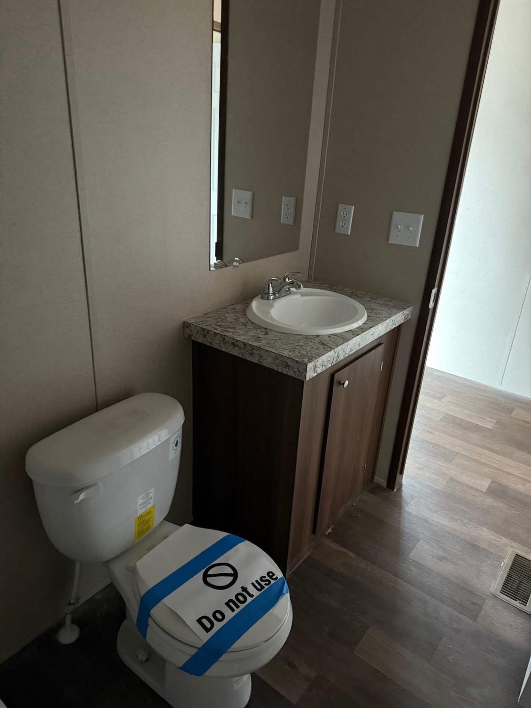 Compact bathroom with a toilet covered by a "Do not use" sign and blue tape. Adjacent is a sink with a marble countertop. Simple and functional setting.