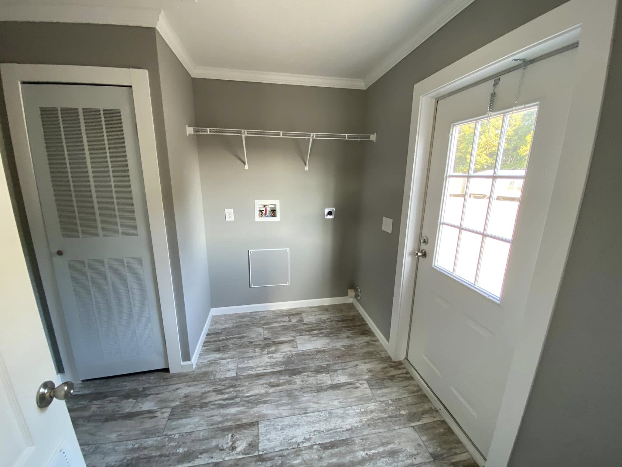 Laundry room with gray walls, a white wire shelf, and a door with glass panels. A louvered closet door and wood-look flooring add a neat, modern touch.