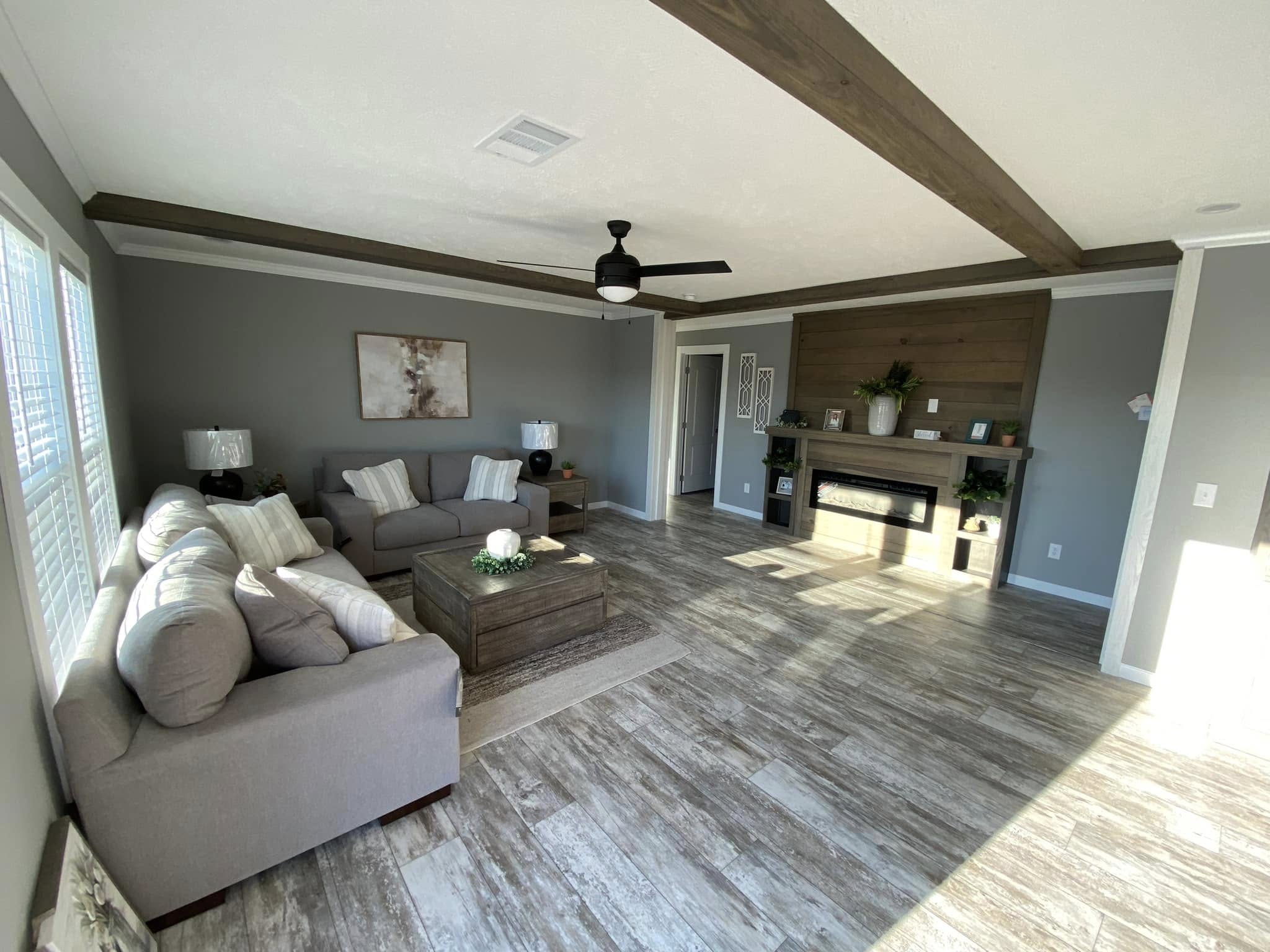 Spacious living room with gray sofas, a wooden coffee table, and a fireplace. Large windows fill the room with light, enhancing the cozy, modern decor.