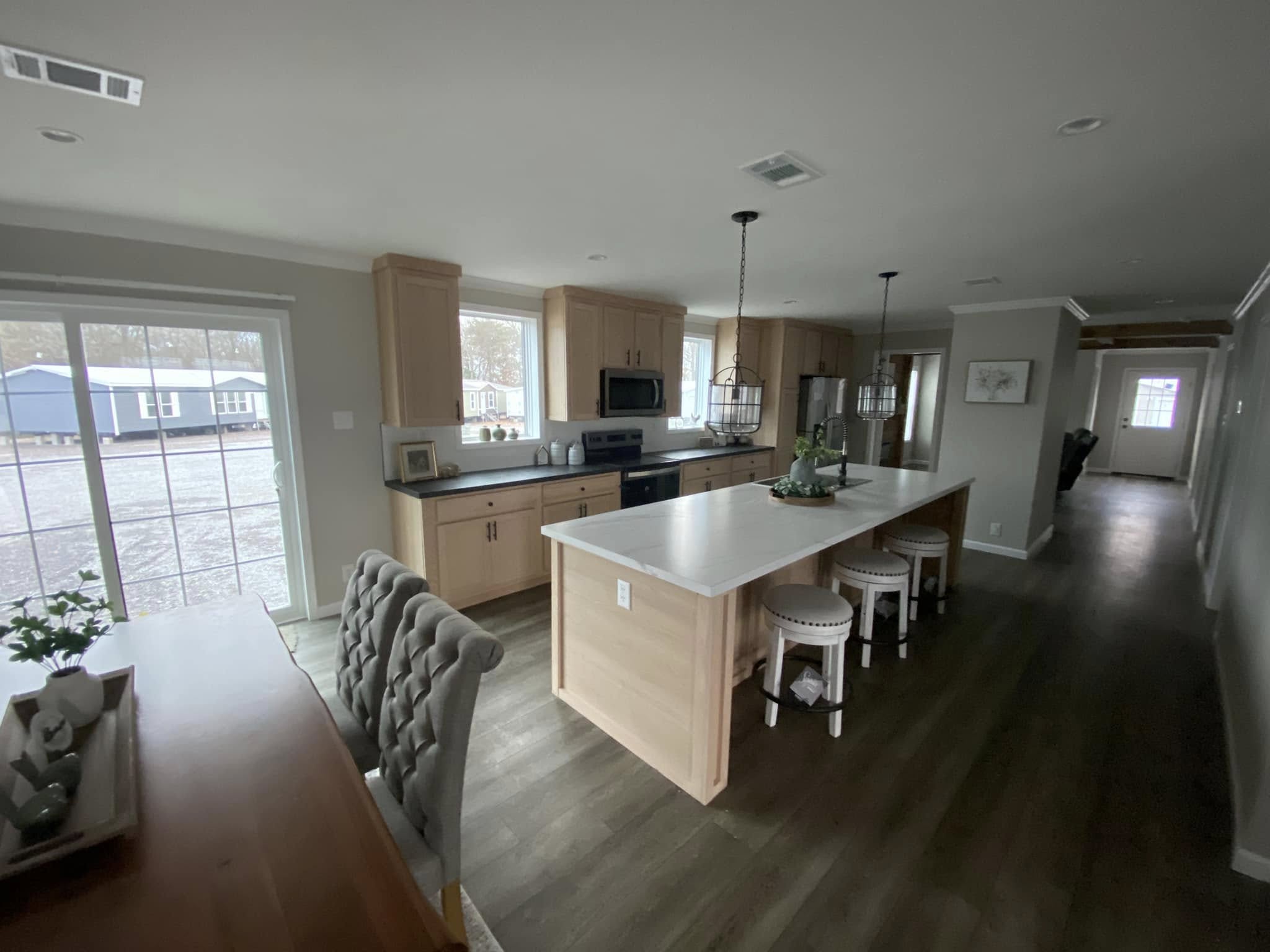 Spacious kitchen with light wood cabinets, a large white island, and stools. Natural light from large windows creates a cozy, inviting atmosphere.