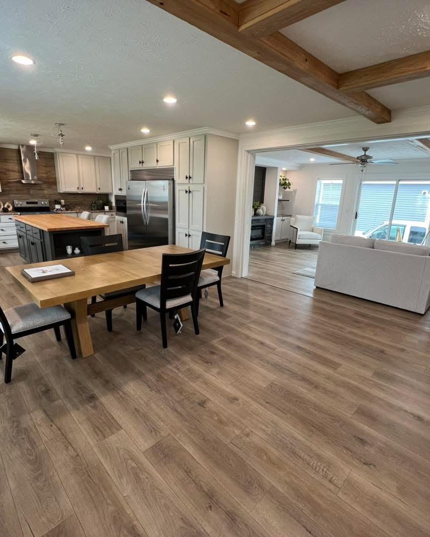Spacious open-plan kitchen and living room with wooden floors. Features a wooden dining table, modern appliances, and cozy couches, conveying a warm, inviting ambiance.
