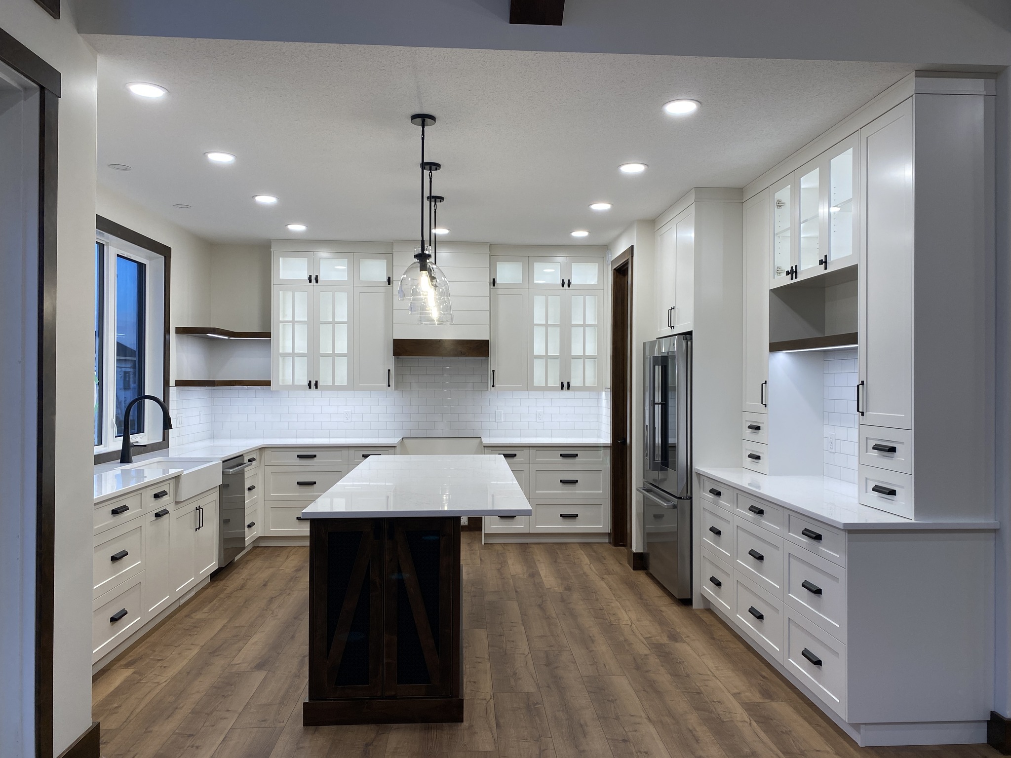 Spacious modern kitchen with white cabinets, a large central island, stainless steel appliances, and wooden floors. Bright, with pendant lights.