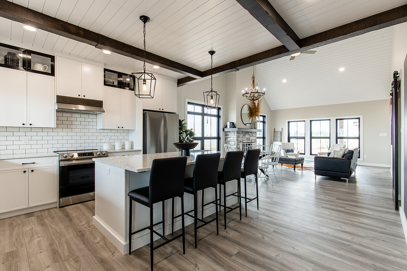 Spacious open-plan kitchen and living room with modern farmhouse decor. Features white cabinets, a large island with black chairs, and cozy seating.