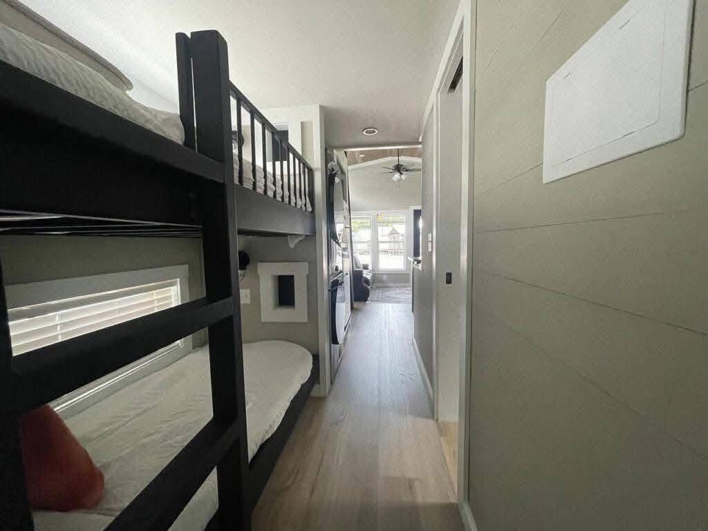 Compact room with bunk beds on the left, a narrow hallway leading to a bright living area with large windows and ceiling fan, creating an airy feel.