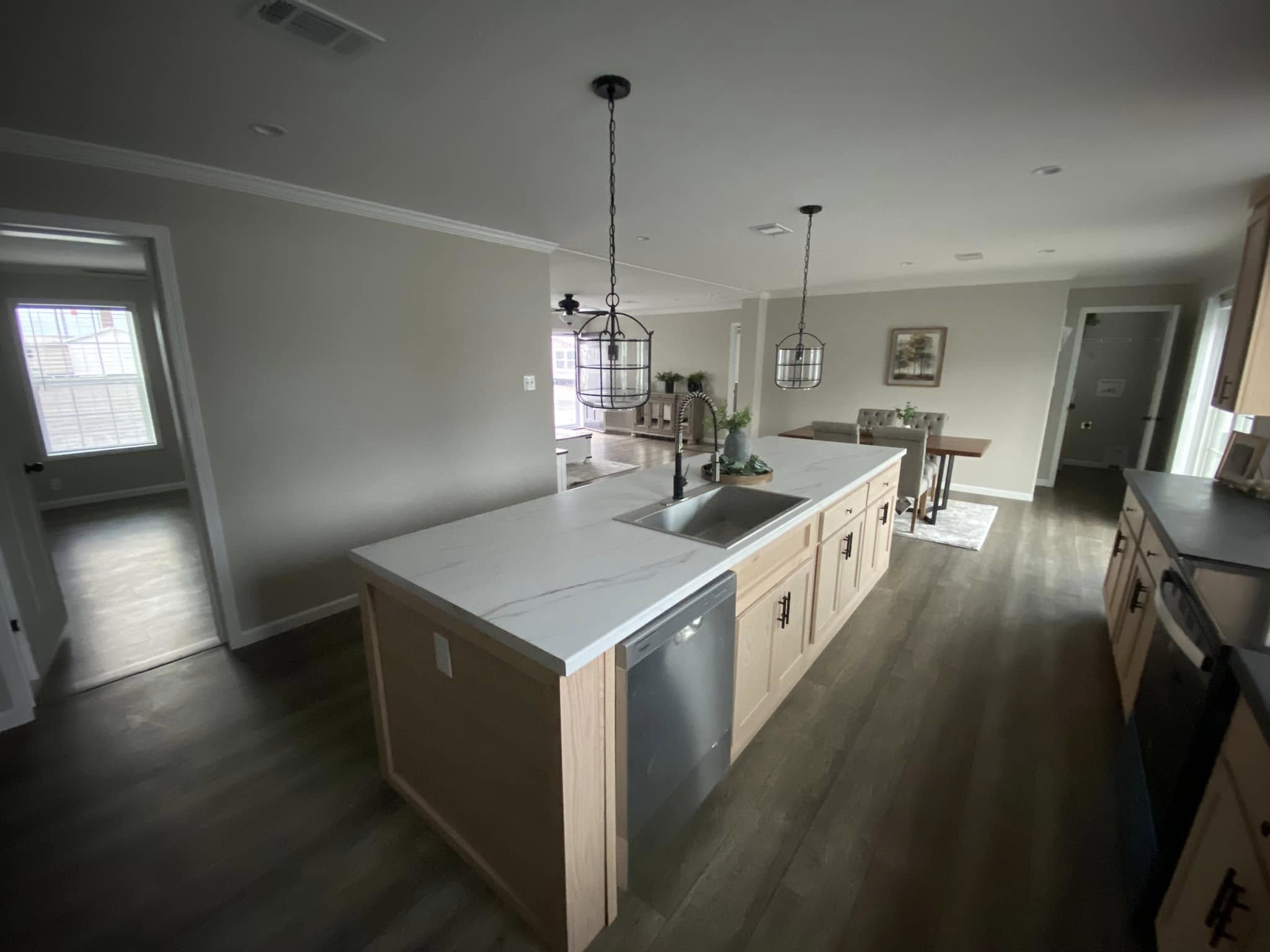 Spacious modern kitchen with a large island, marble countertops, and pendant lights. Light wood cabinets and dining table create a welcoming, airy feel.
