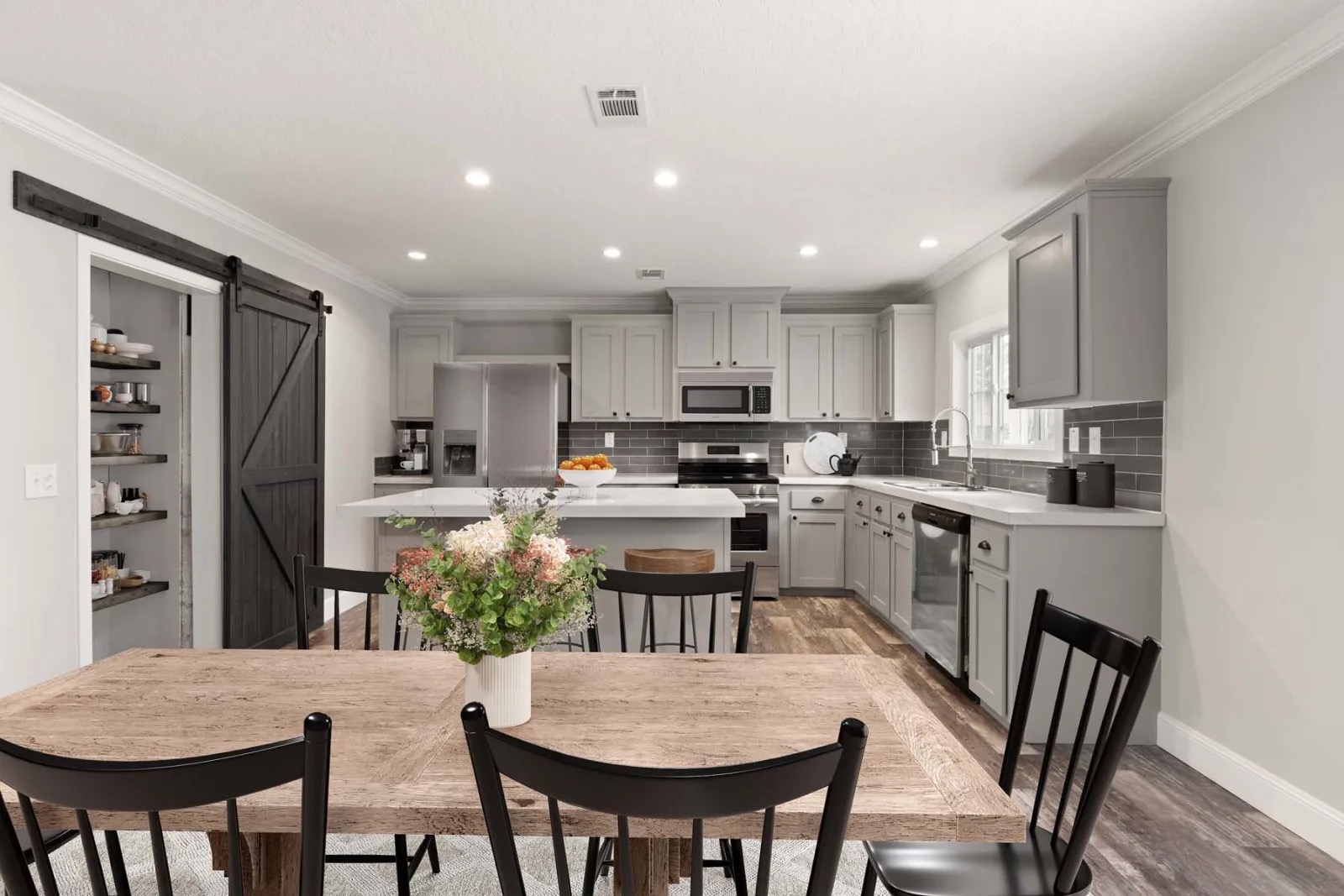 Spacious kitchen with gray cabinets, white countertops, and stainless steel appliances. A rustic dining table with flowers and black chairs adds warmth.