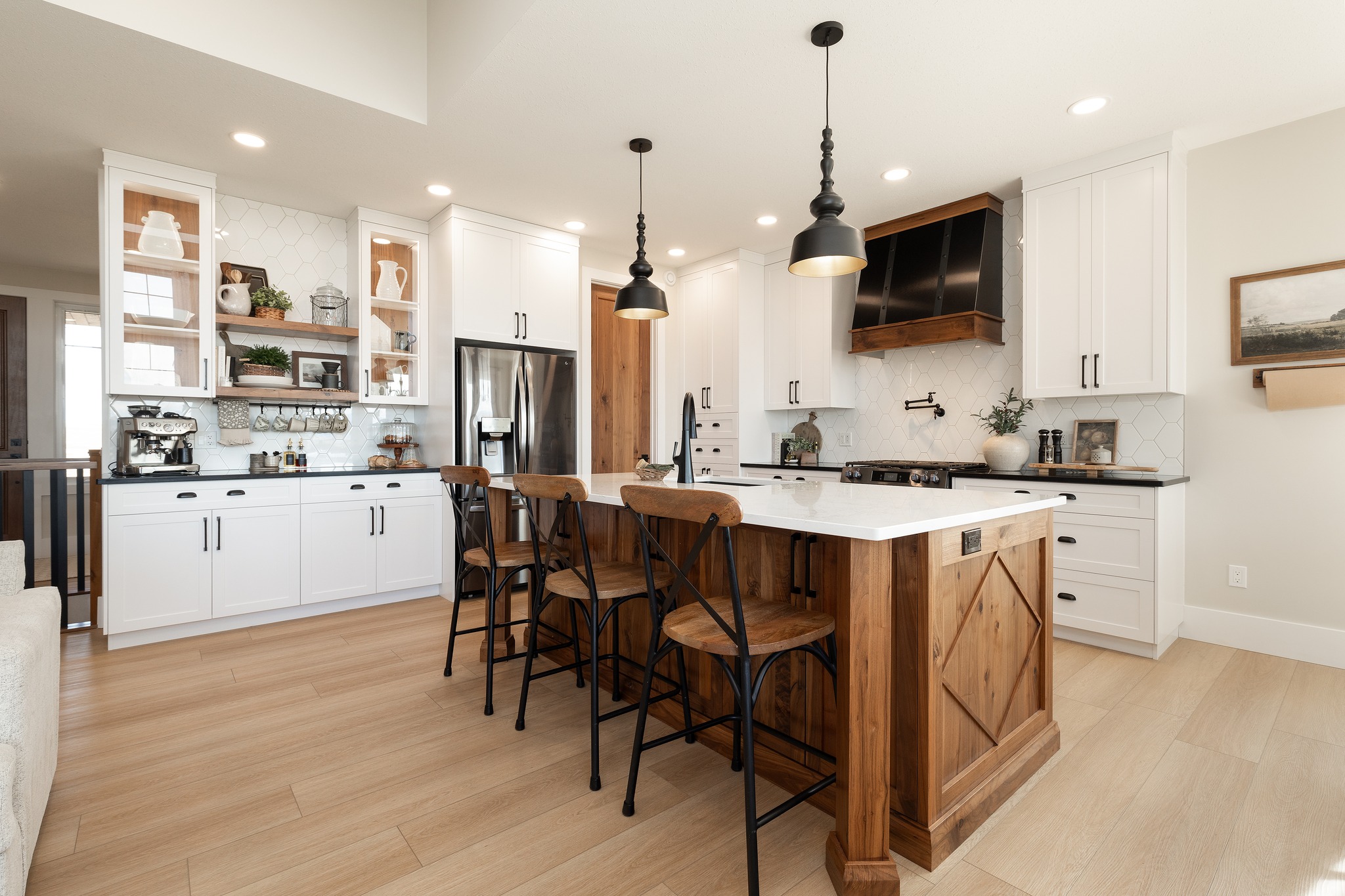 Modern kitchen with white cabinets, a large wooden island, black pendant lights, and stainless-steel appliances. Warm, inviting atmosphere.