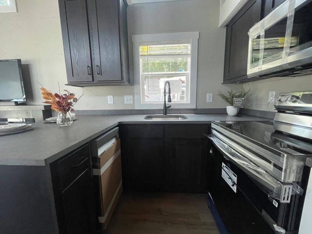 Compact modern kitchen with dark cabinets, a stainless steel oven, and black faucet. A vase with autumn leaves adds a touch of warmth.