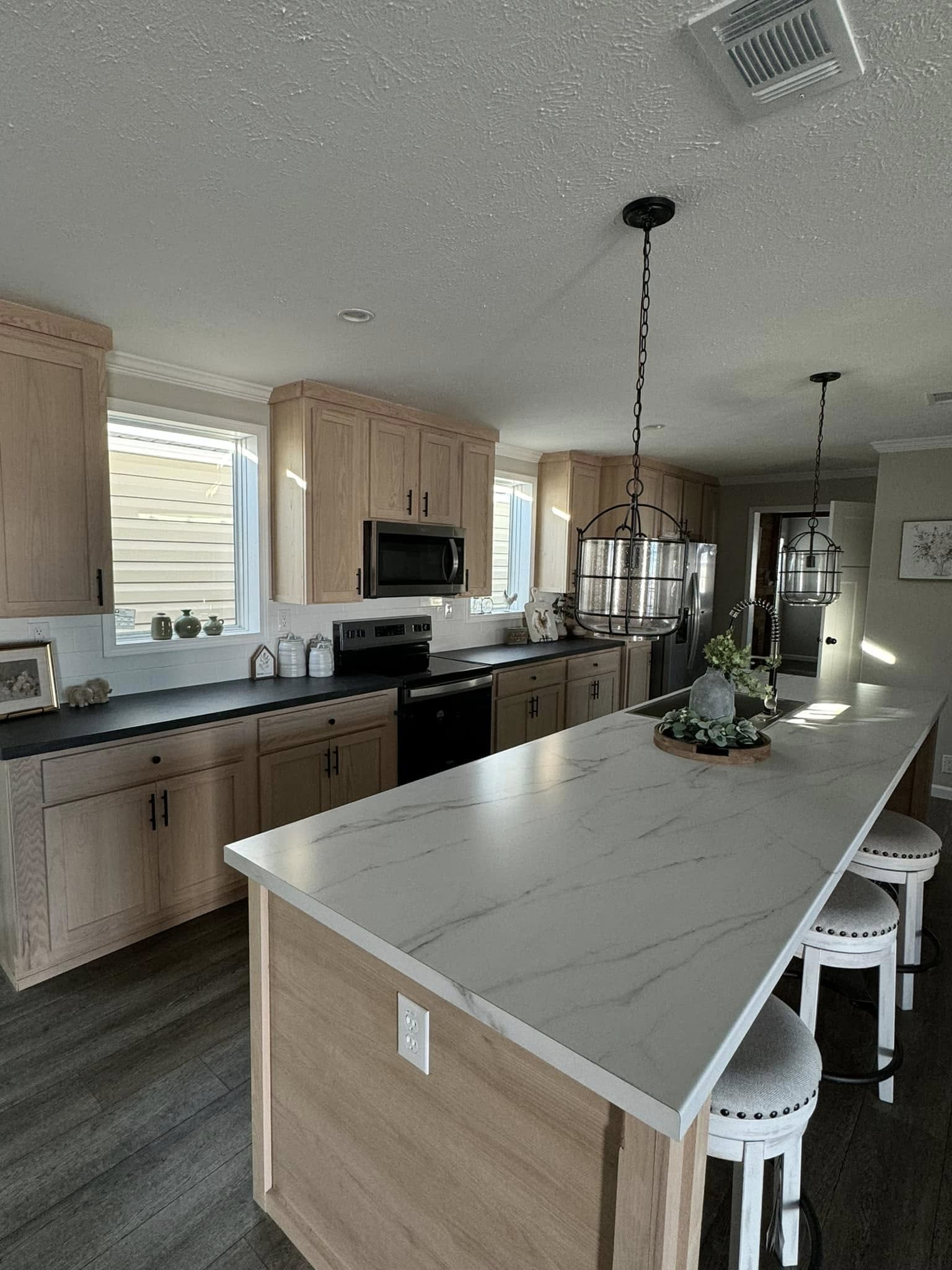 Modern kitchen with wooden cabinets, a large white marble island, and bar stools. Pendant lights hang above, adding warmth and elegance.