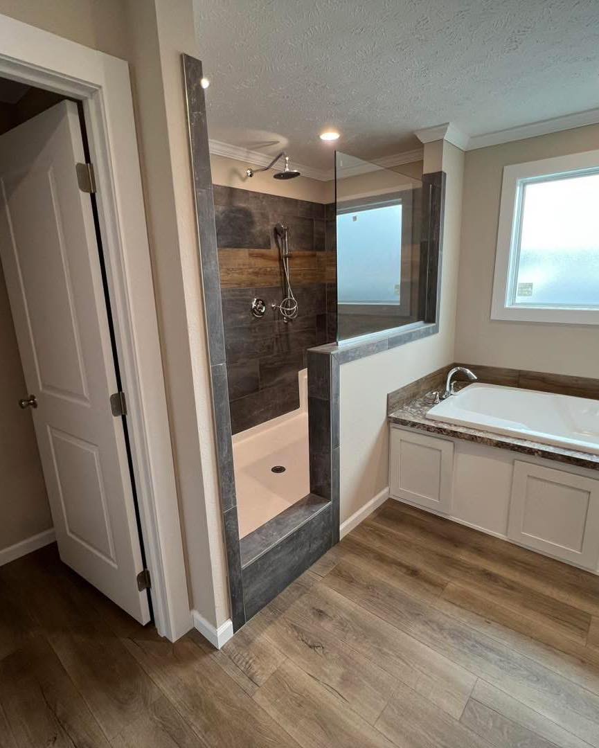 Modern bathroom featuring a walk-in shower with gray tiles, a large bathtub with marble countertops, and wood-style flooring, evoking a calm, elegant vibe.