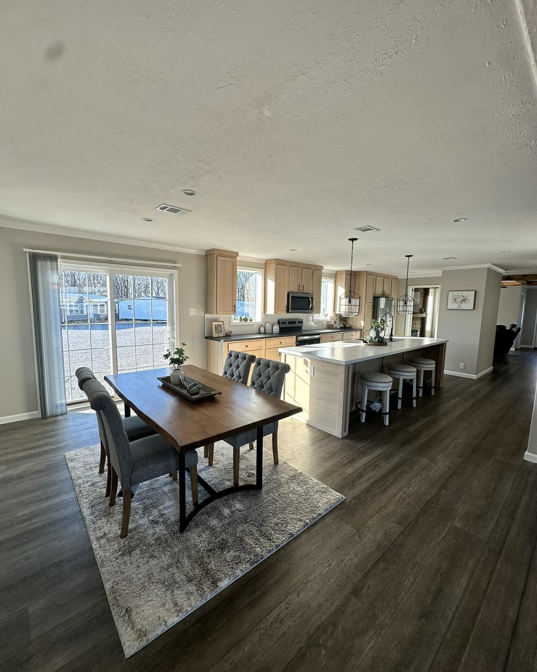 Spacious open-plan kitchen and dining area with wood floors. Features a modern island, wooden cabinets, dining table, and large windows with garden view.
