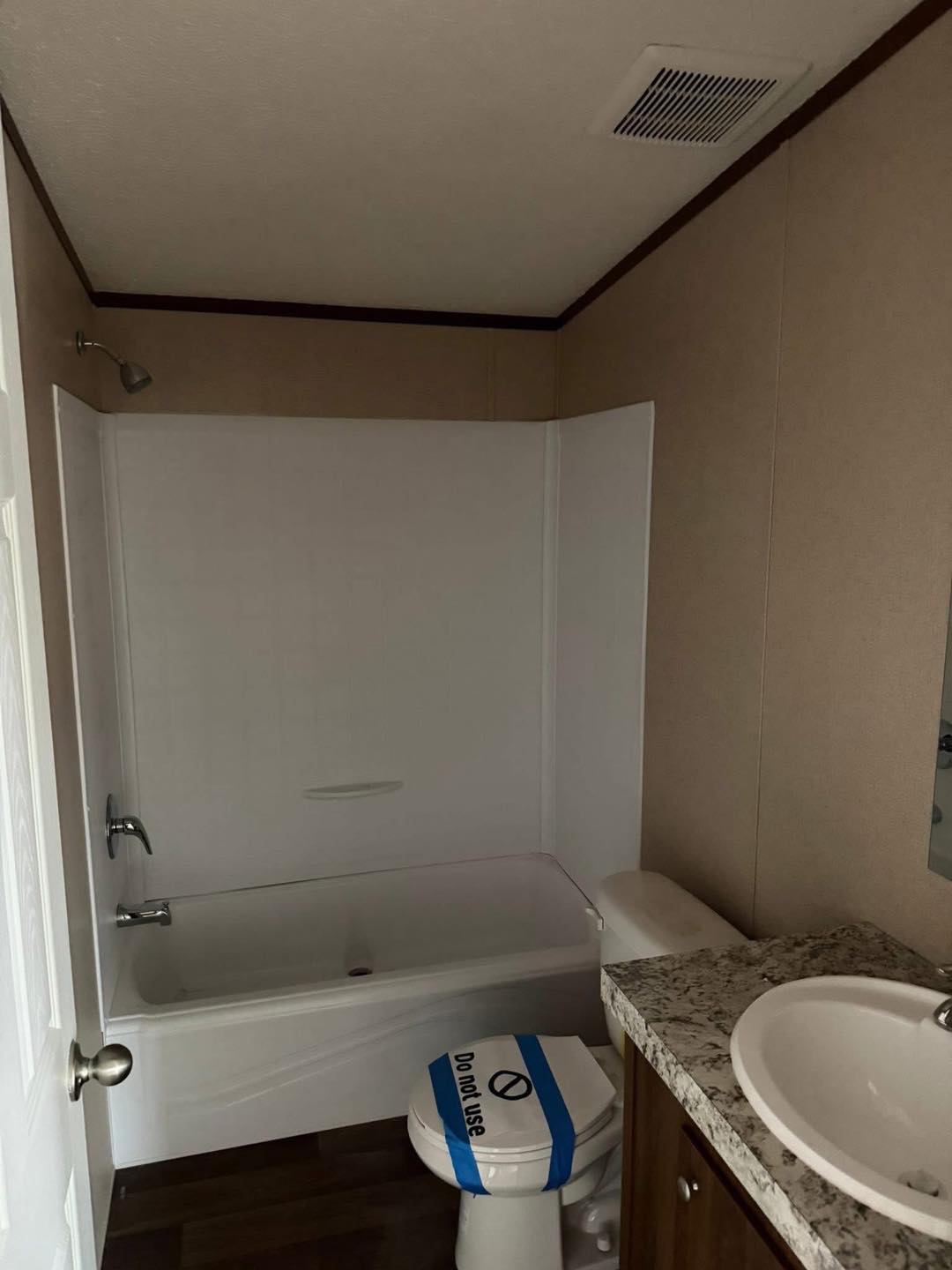 A small bathroom with dim lighting features a bathtub with a shower, a toilet labeled "Do not use," and a beige countertop with a round sink.