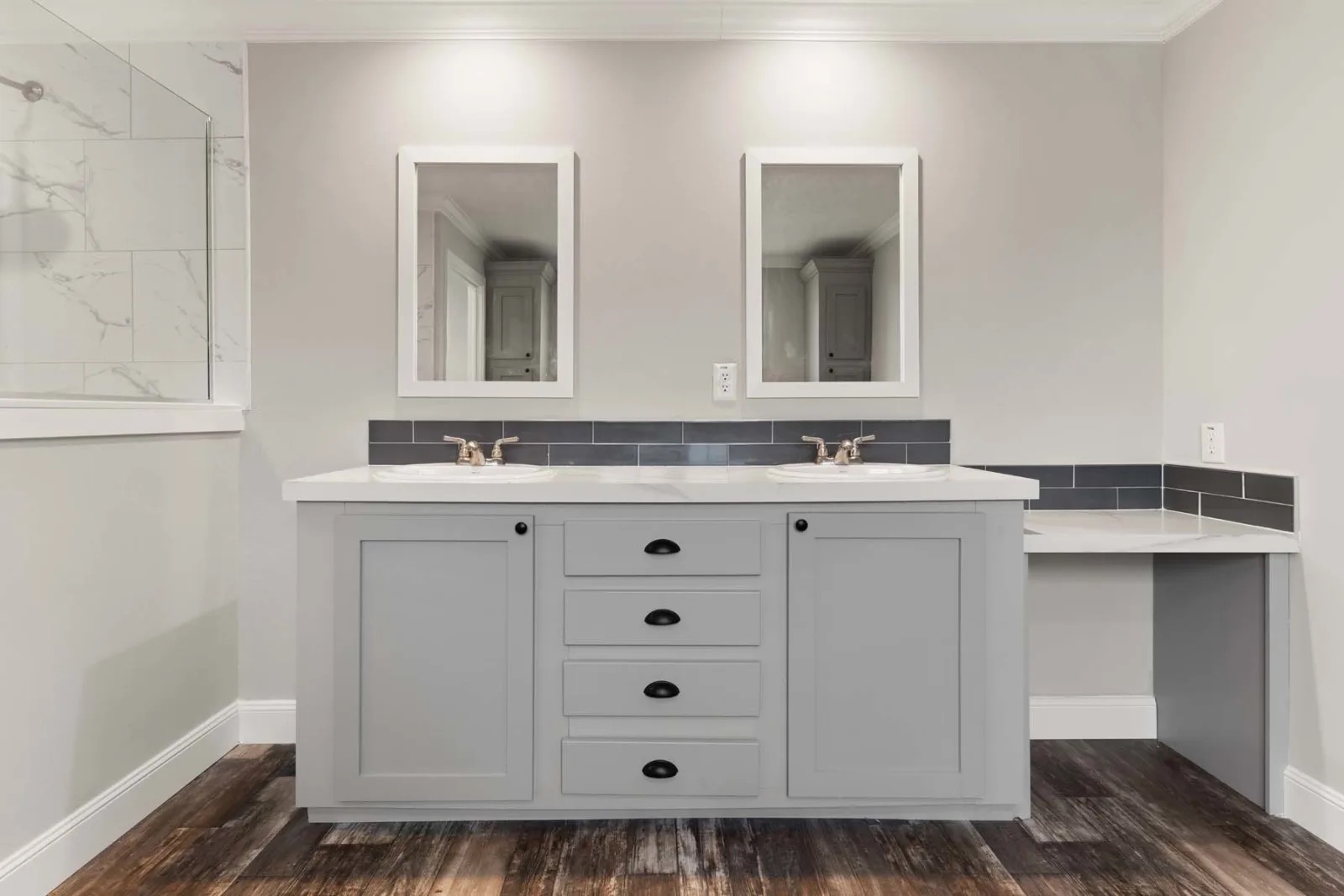 Modern bathroom with a double vanity featuring two mirrors and sinks. Gray cabinets and a rich wood floor create a clean, elegant look.