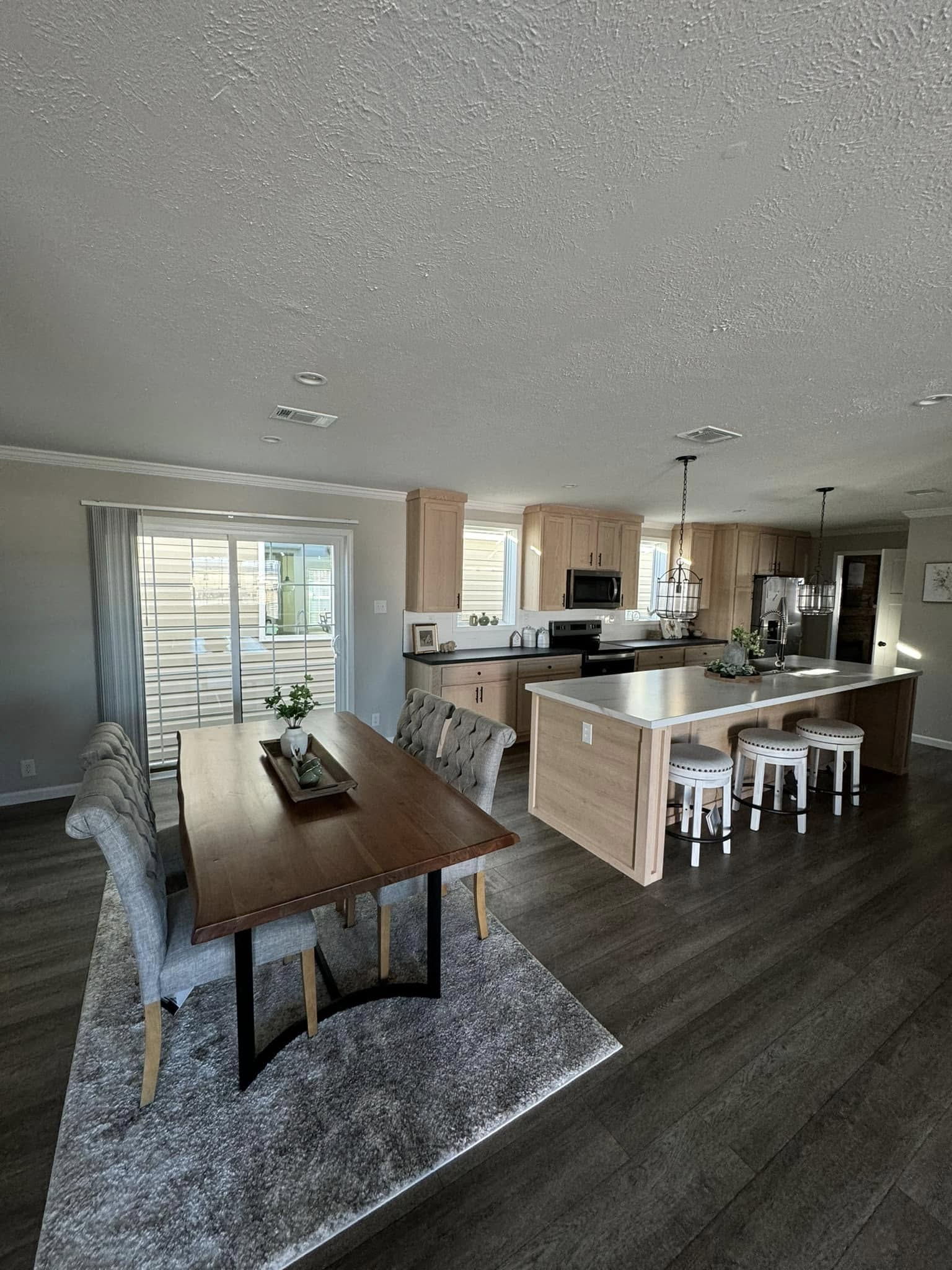 Spacious modern kitchen and dining area with wood floors. A wooden dining table with cushioned chairs is on a rug; kitchen island with stools nearby. Brightly lit.