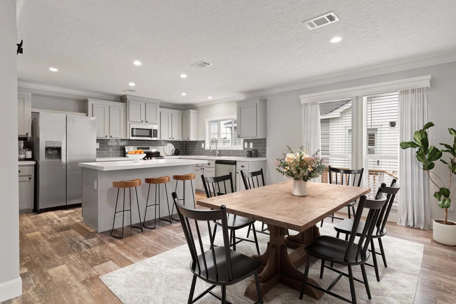A modern kitchen with gray cabinets, white countertops, and stainless steel appliances. A basket of vibrant fall flowers adds warmth on the island.