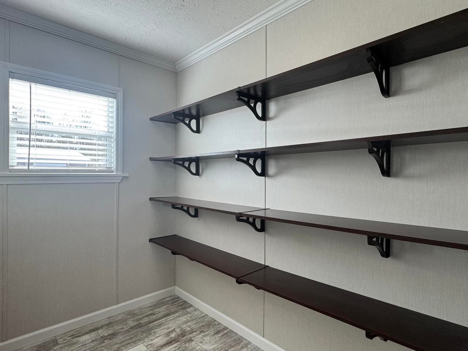 Room with wooden shelves on beige walls, supported by black brackets. A small window on the left wall lets in light, creating a minimalist tone.