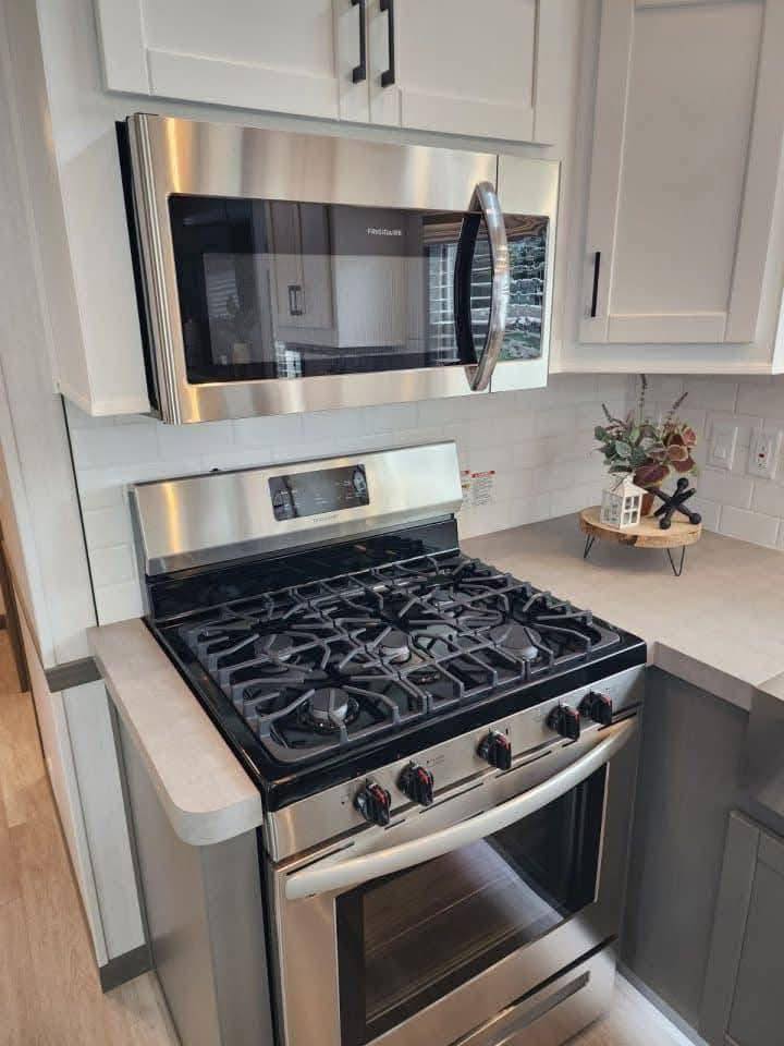 Modern kitchen featuring stainless steel appliances; a stove with black grates and dials below a microwave. White cabinets and a minimal decor accent.
