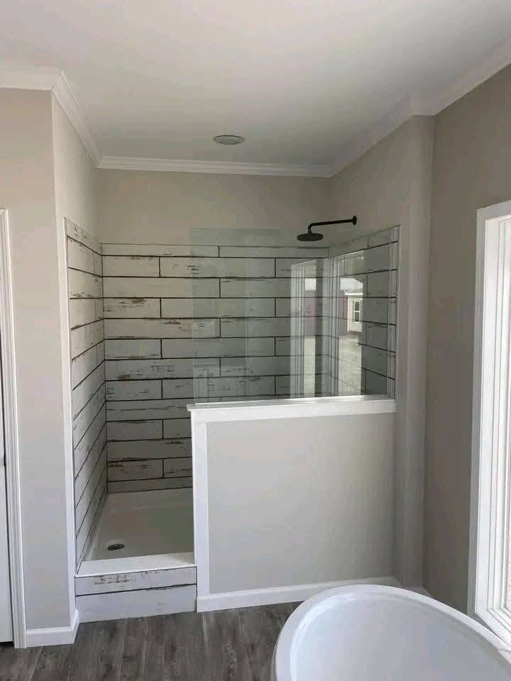 Modern bathroom with a white tiled shower featuring rustic wood-look walls and a glass partition. Light gray walls and hardwood floors enhance calmness.