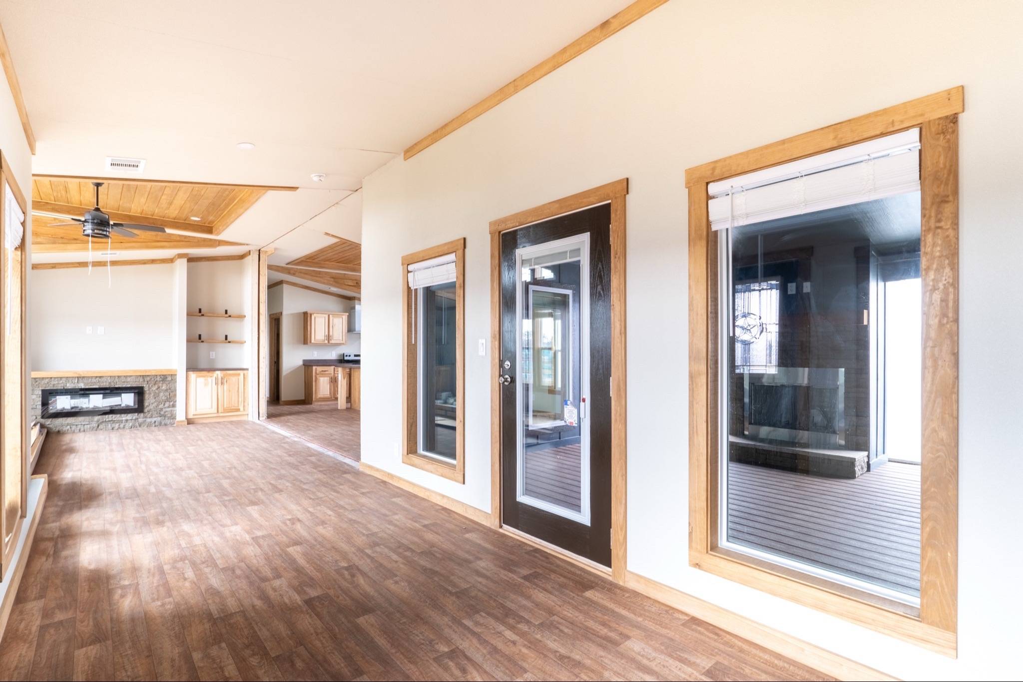 Spacious hallway with wood flooring, large windows, and a glass door on the right. A cozy fireplace and kitchen with wood cabinets are visible ahead.
