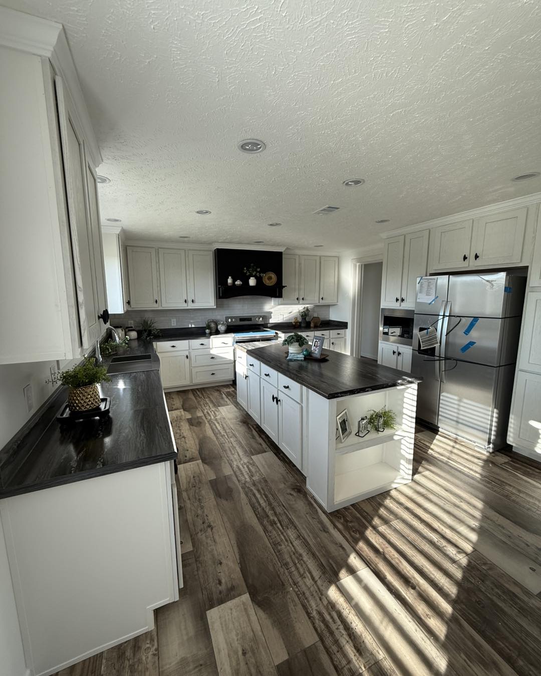 Spacious living room with wood accents and large windows. Features a light gray couch, ceiling fan, fireplace, and a wooden coffee table, offering a cozy ambiance.