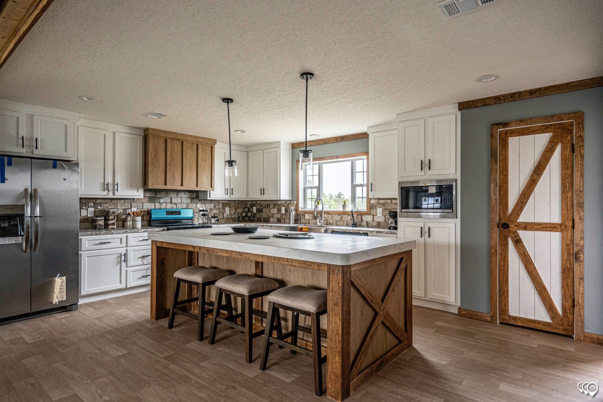 Rustic kitchen with a large island featuring wooden accents and three stools. White cabinets, stainless steel appliances, and a barn-style door. Cozy and inviting.
