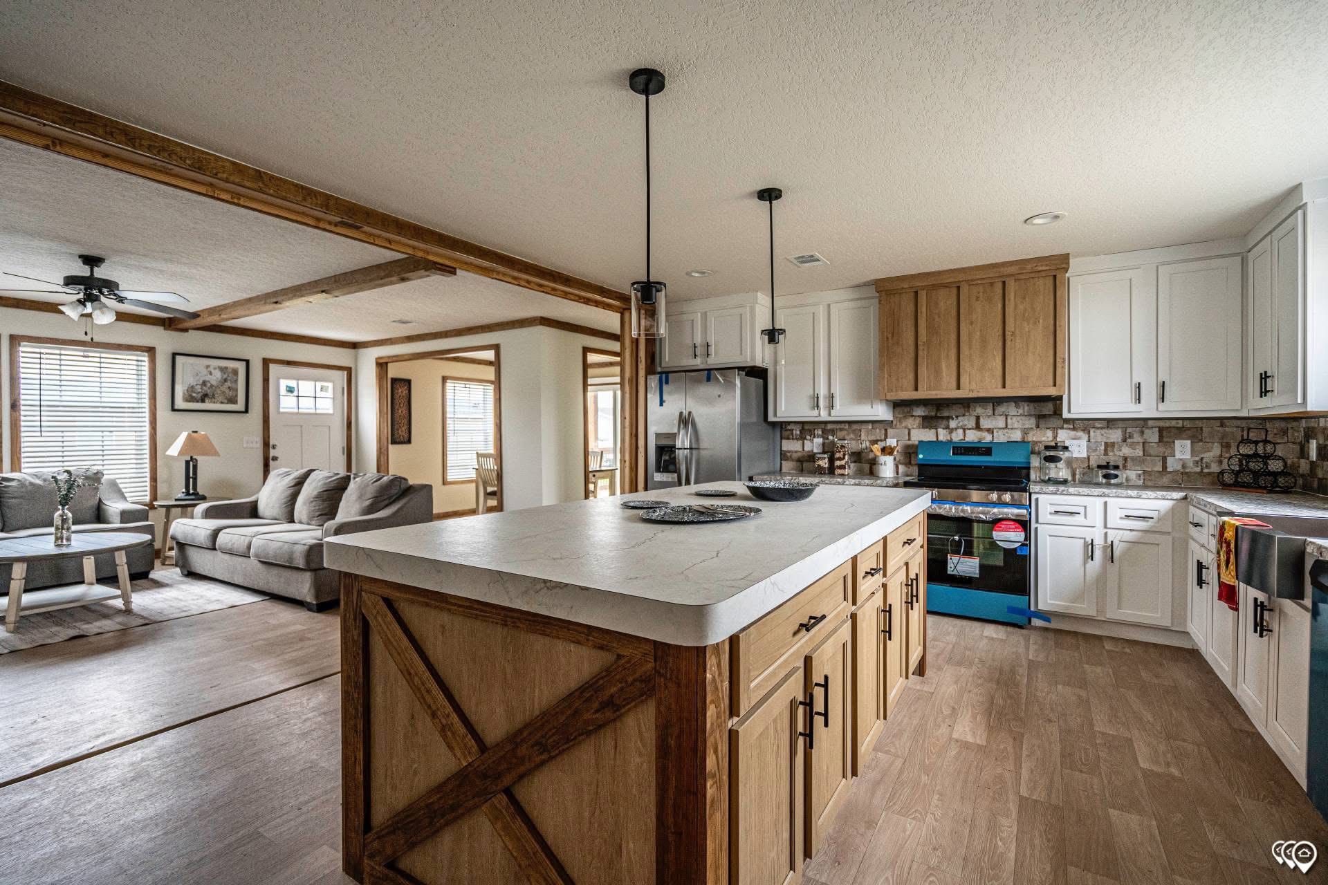 Spacious kitchen and living area with rustic charm. Features a large island with wooden cabinets, modern appliances, cozy sofa, and wooden beams.