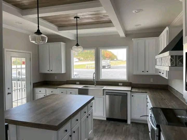 A modern kitchen with white cabinets, wooden countertops, and stainless steel appliances. Two pendant lights hang above a central island. Large windows illuminate the space.