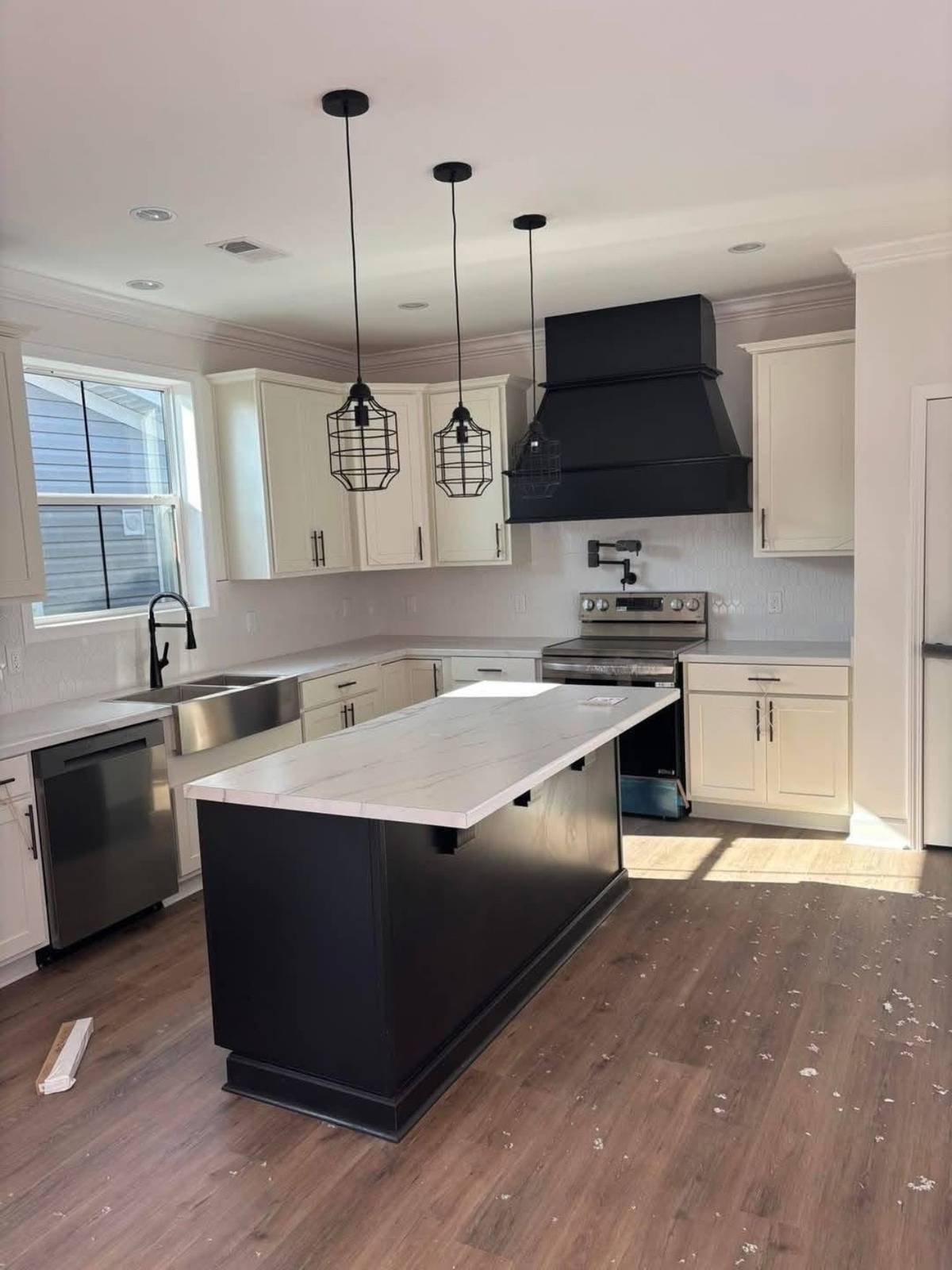 Modern kitchen with white cabinets, black appliances, and a central island with a marble countertop. Three hanging pendant lights add elegance.