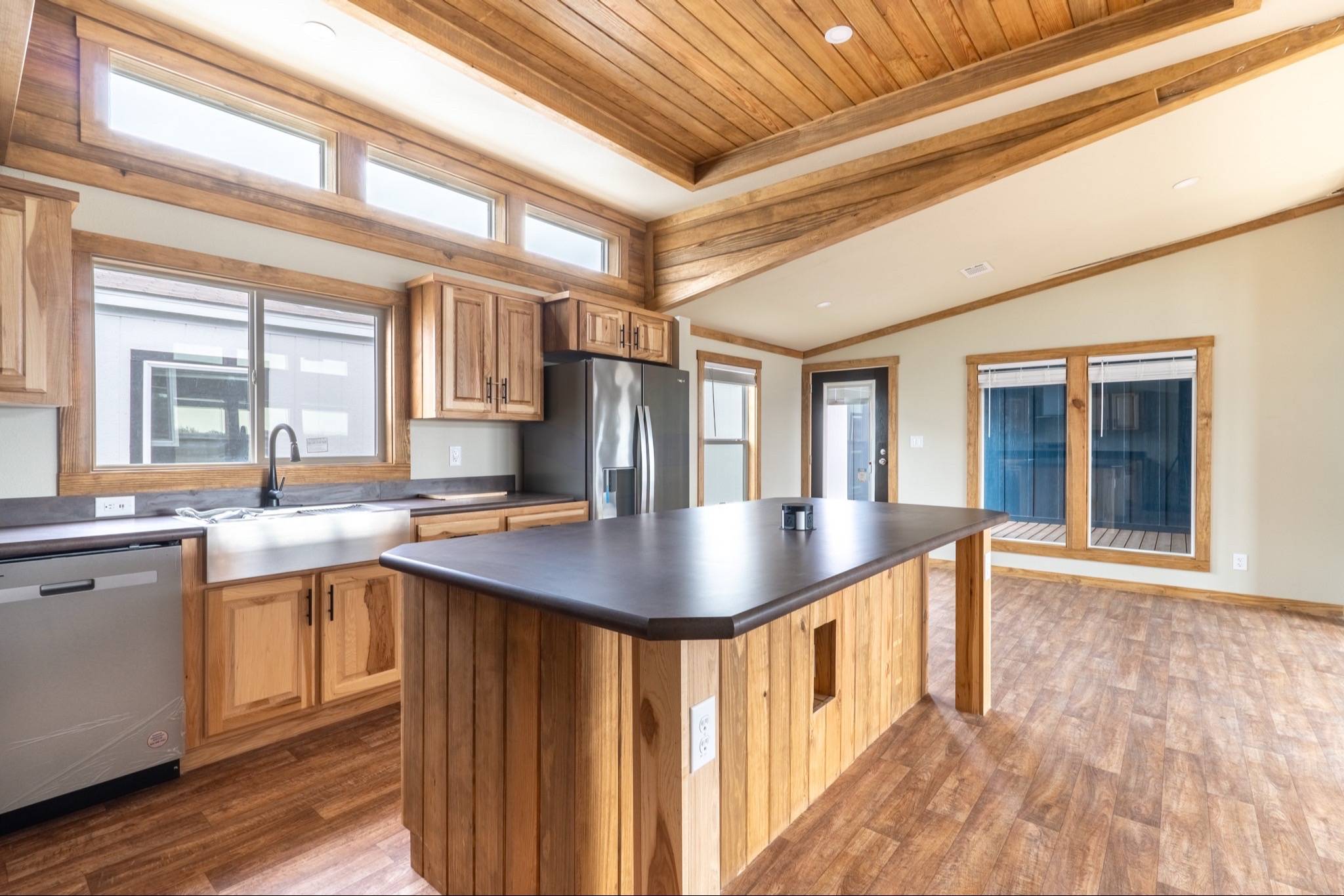 Spacious kitchen with rustic wooden cabinets and ceiling, a large island, stainless steel appliances, and ample natural light from high windows.