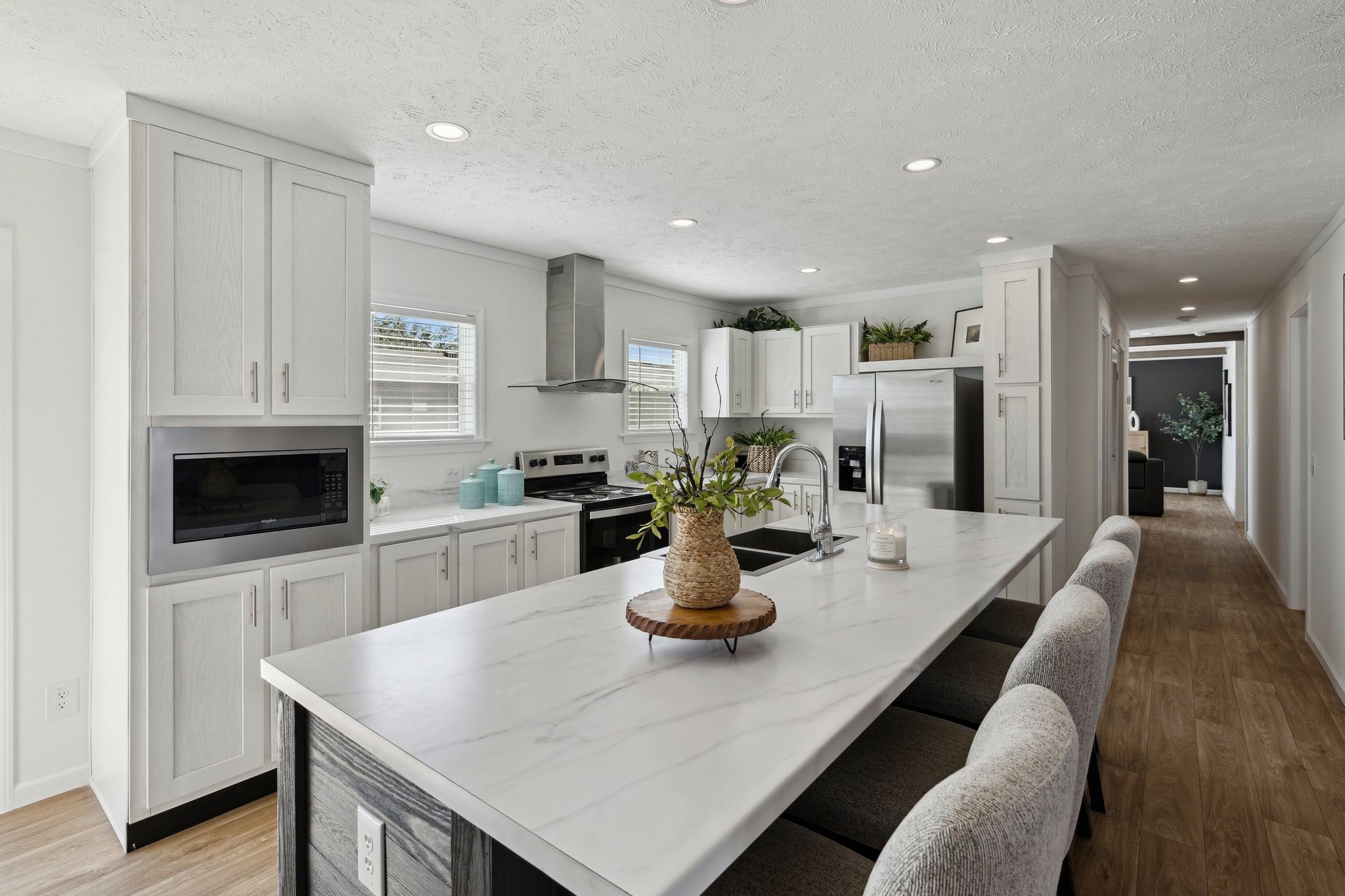 Modern kitchen with a marble island, gray bar stools, stainless steel appliances, and white cabinets. Bright, airy atmosphere with wood flooring.