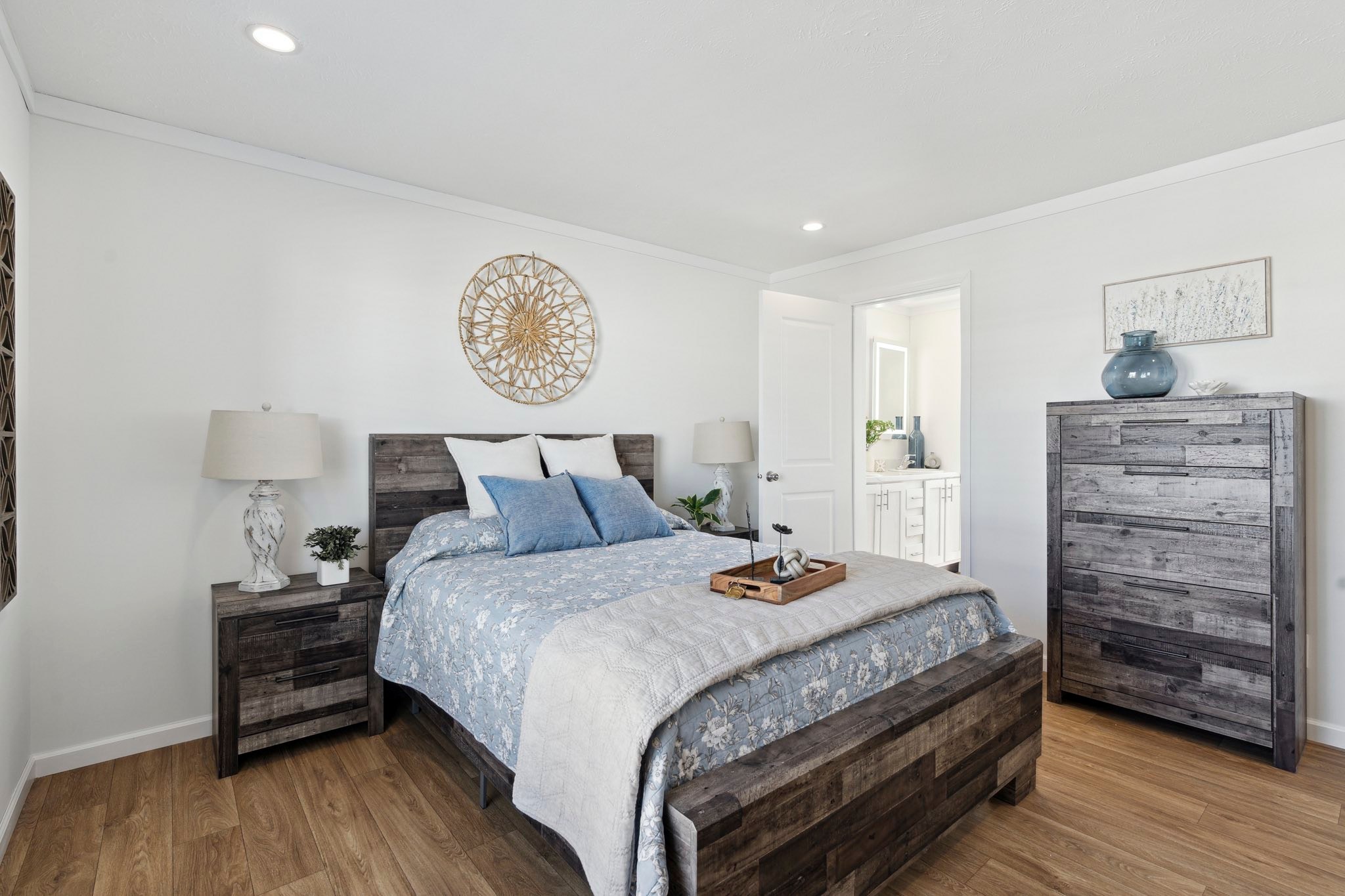 Cozy bedroom with a rustic wood bed, adorned with blue bedding and pillows. Two lamps on side tables, a decorative tray, and a wall art piece add charm.