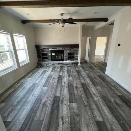 Spacious living room with gray wood flooring, white walls, and ceiling beams. A modern fireplace flanked by built-in shelves adds a cozy touch.