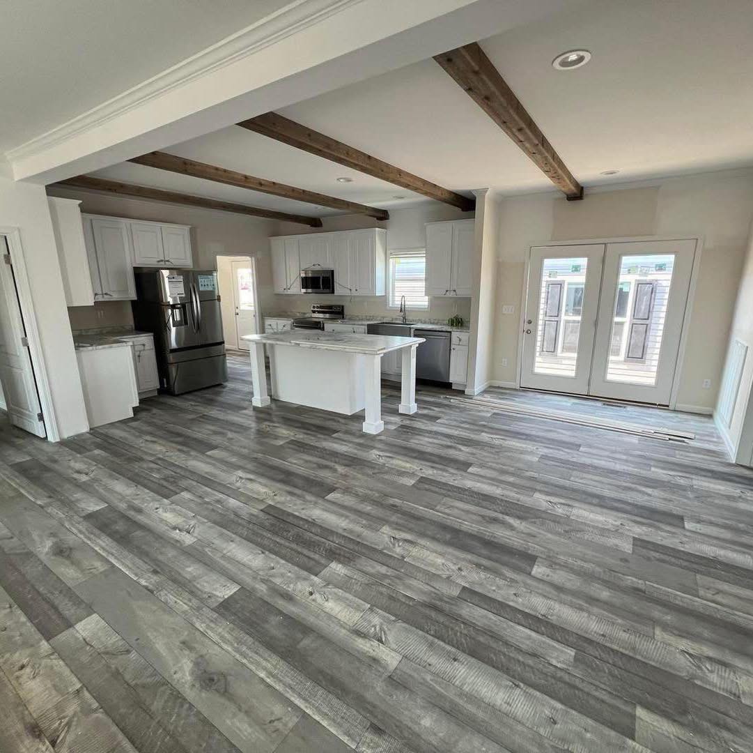 Modern kitchen with gray wood floors, white cabinetry, and a marble island. Exposed wooden beams add warmth. French doors bring in natural light.