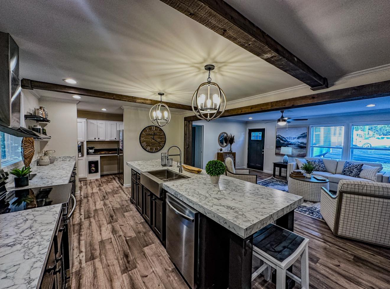 Modern kitchen and living area with a cozy, open-plan design. Features wooden floors, marble countertops, stylish lighting, and comfortable seating. Warm ambiance.