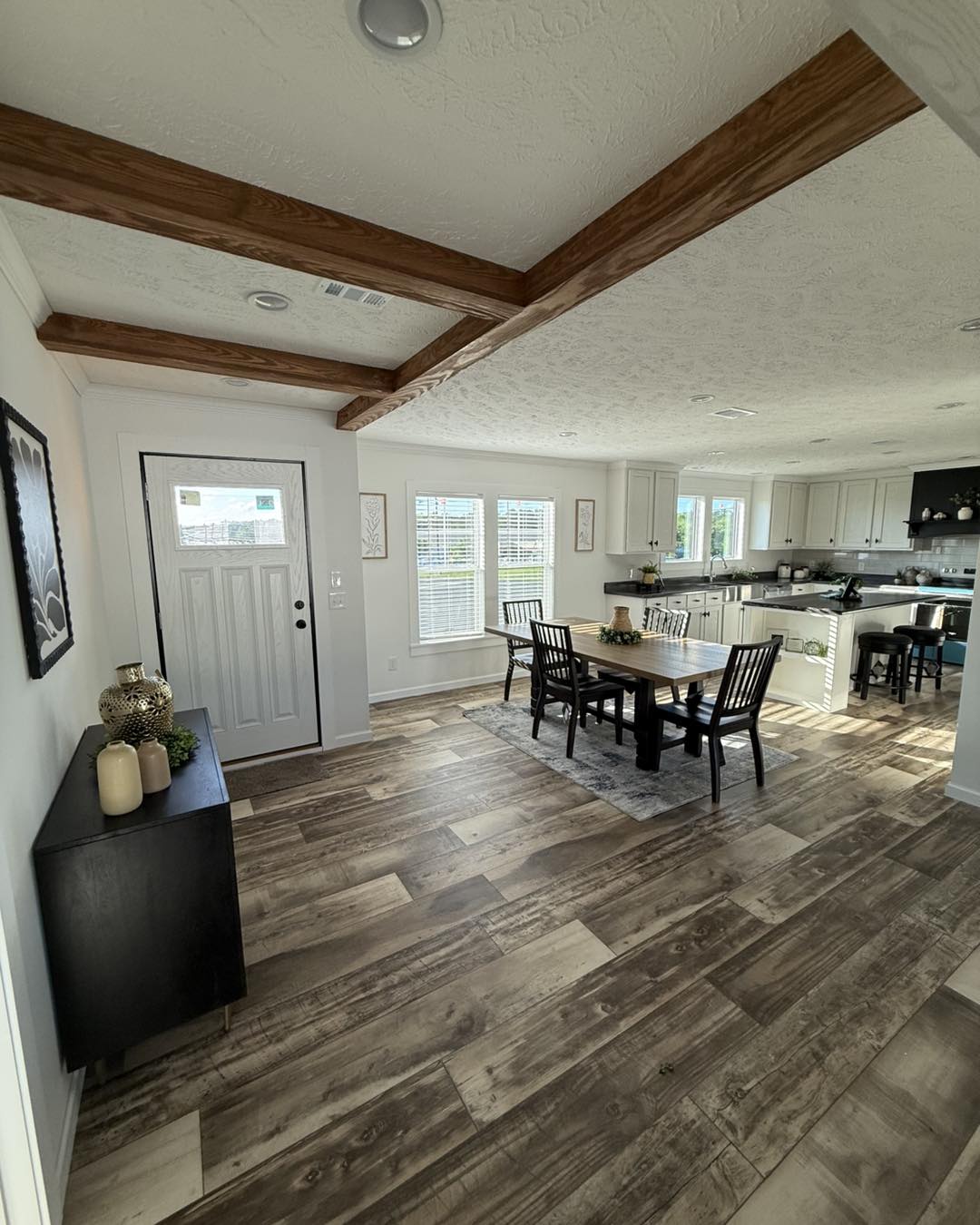 Spacious open-concept kitchen and dining area with rustic wooden beams and light wood floors. Natural light streams through large windows, creating a warm, inviting atmosphere.