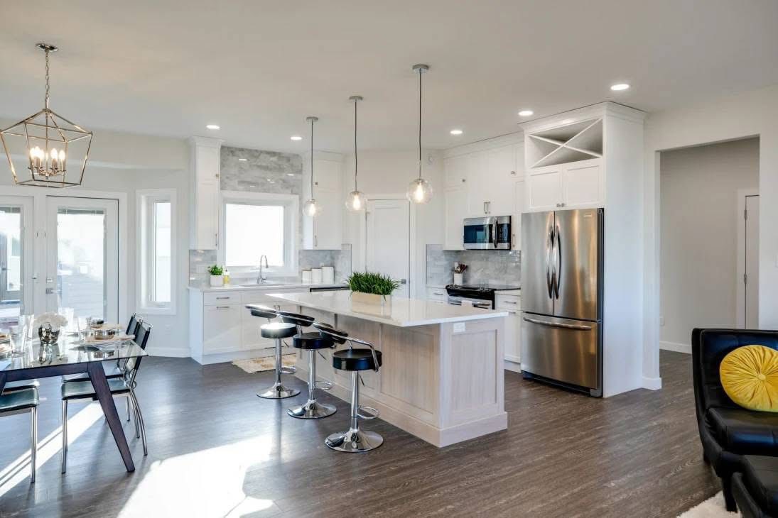 Modern kitchen and dining area with a large island, black bar stools, stainless steel appliances, dark wood flooring, and pendant lighting.